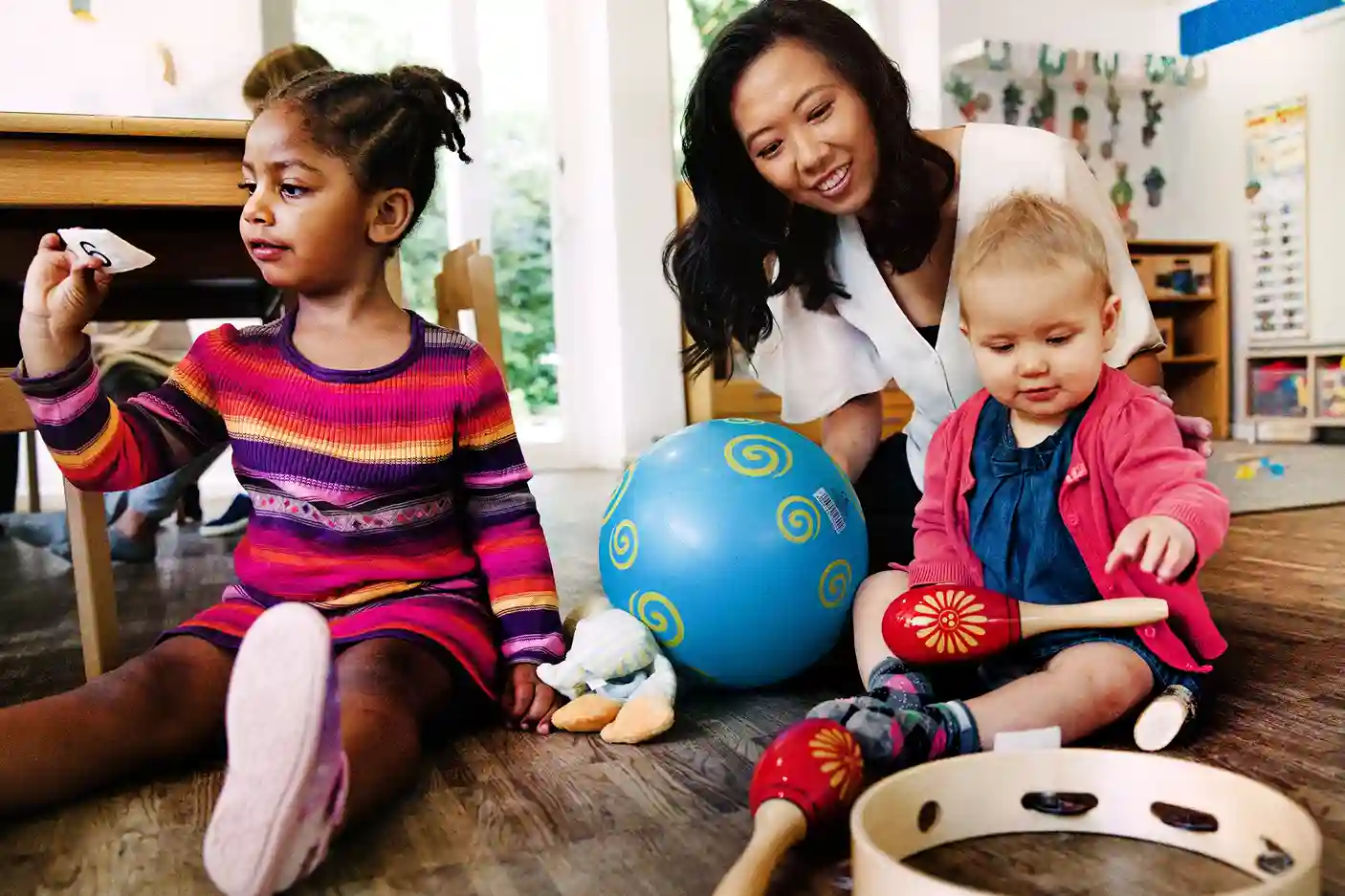 Kind spielt mit Erzieherin und anderen Kindern an Musikinstrumenten